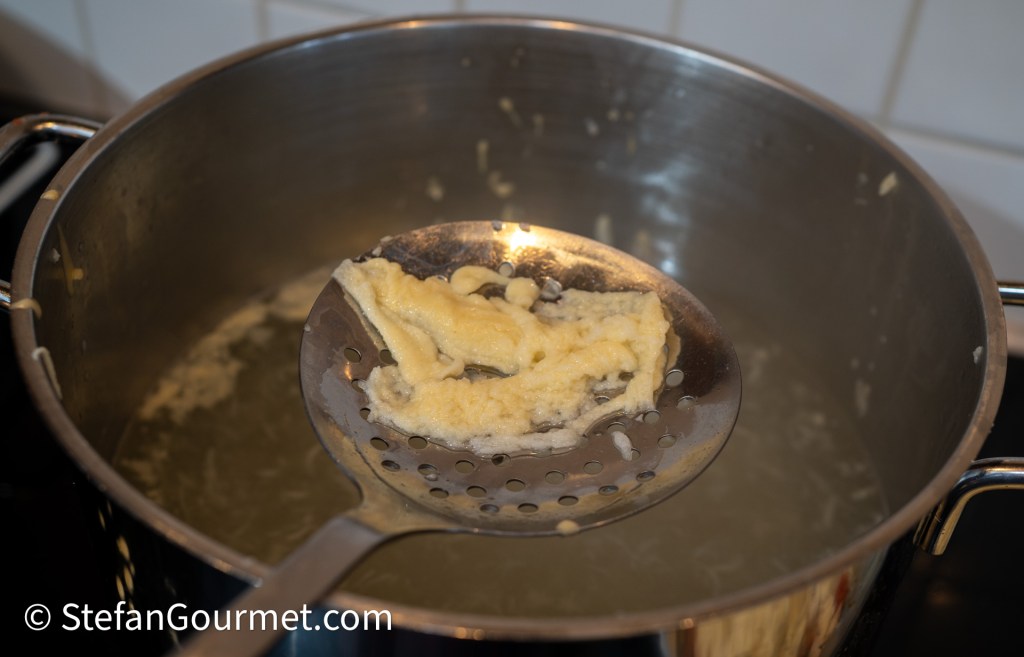 A slotted spoon holding freshly cooked girini pasta above a pot of boiling water.