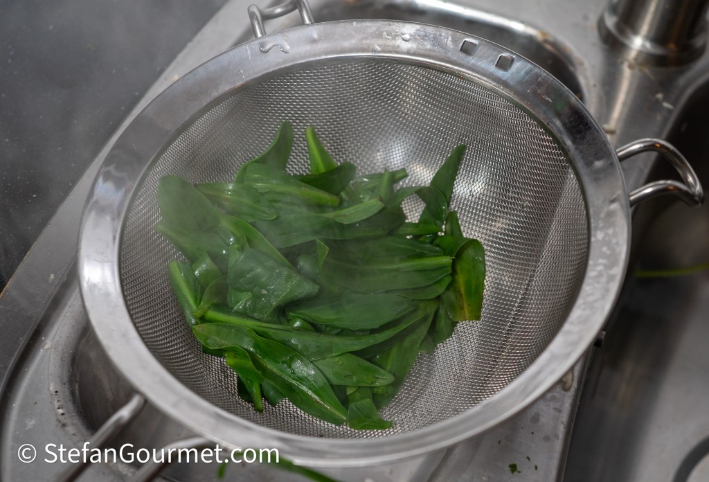 Fresh sea lavender leaves being blanched in boiling water and drained in a mesh strainer.
