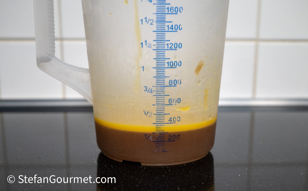 Measuring jug with layers of liquid, including stock and oil, displayed on a dark surface.