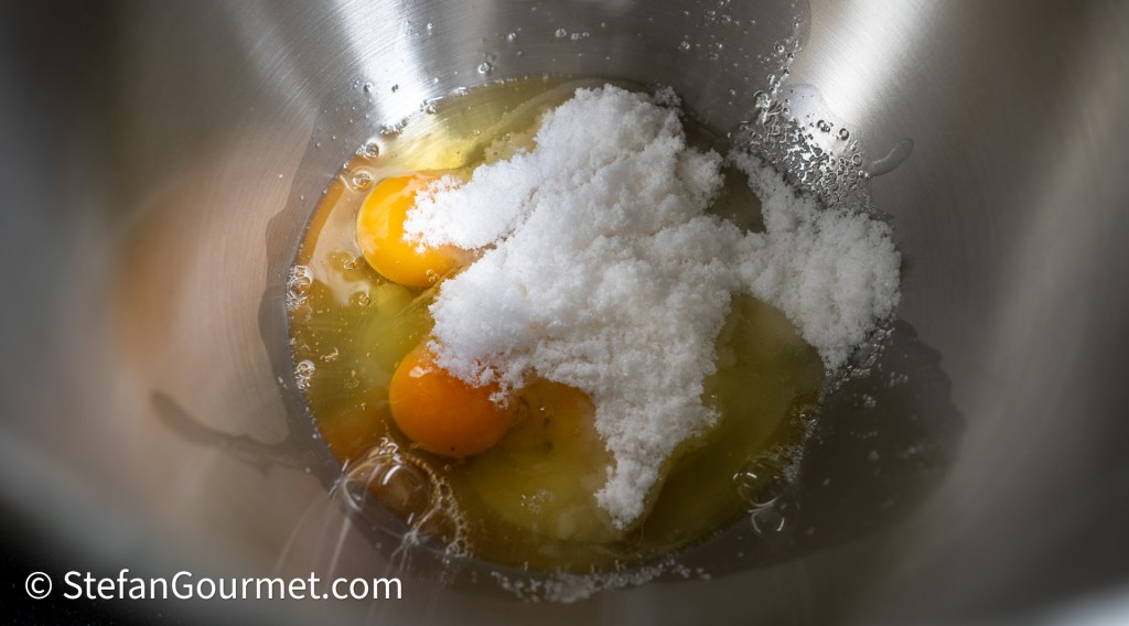 A mixing bowl containing two egg yolks, sugar, and liquid egg whites, ready for whisking.