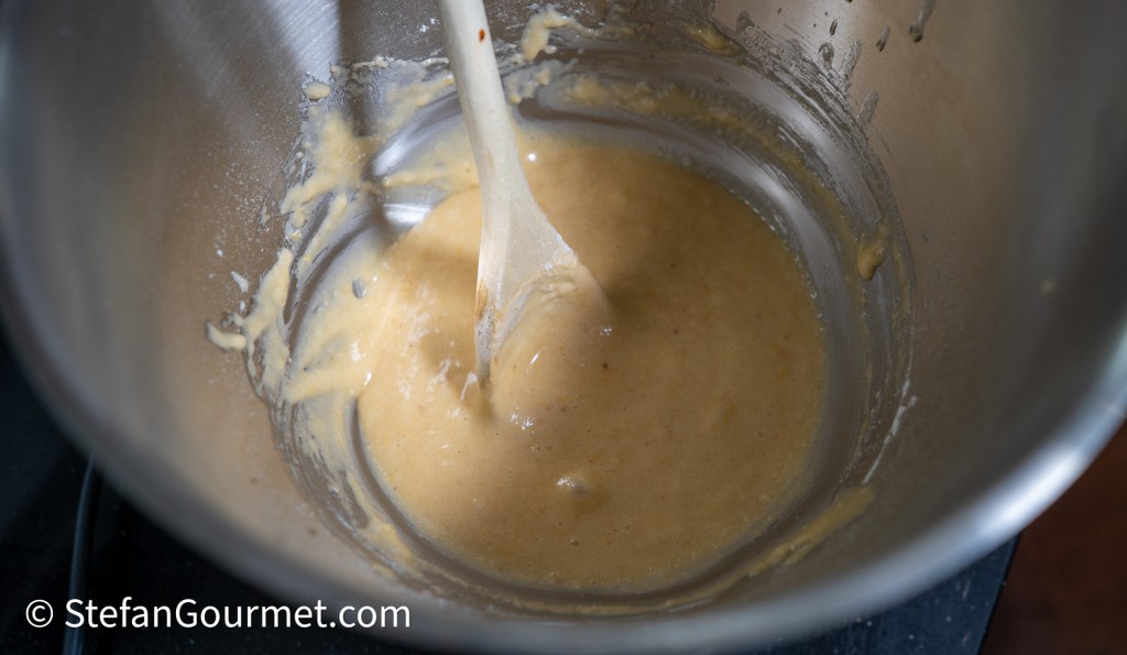 Batter for raspberry and almond cake in a stainless steel mixing bowl, stirred with a wooden spoon.