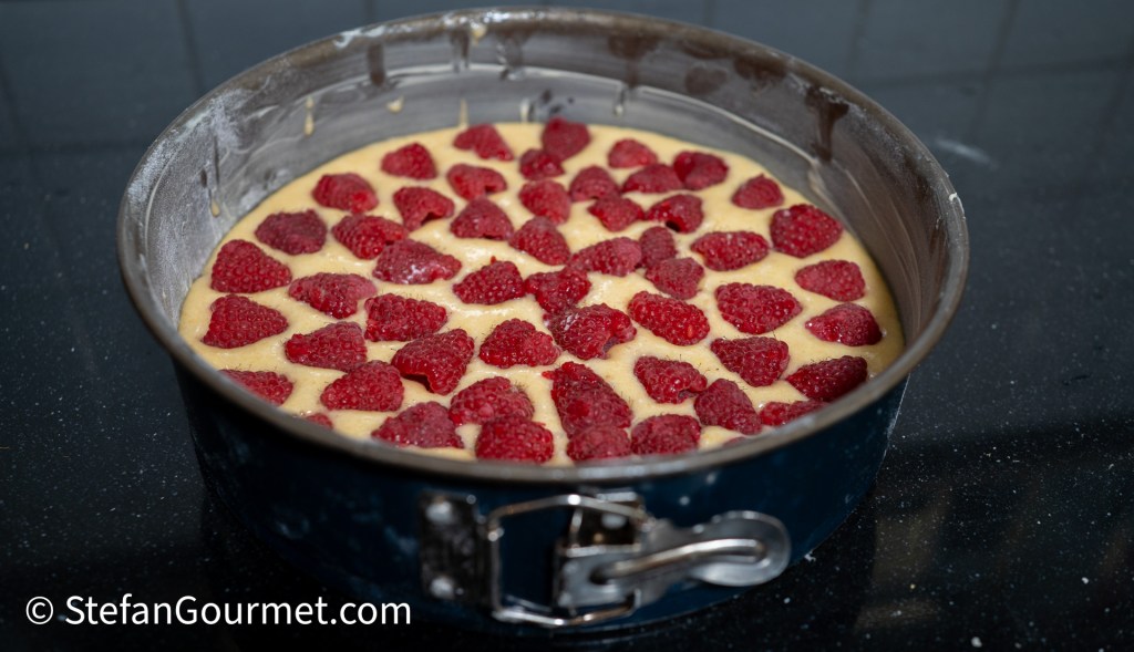 Raspberry almond cake batter in a springform pan topped with fresh raspberries, ready for baking.
