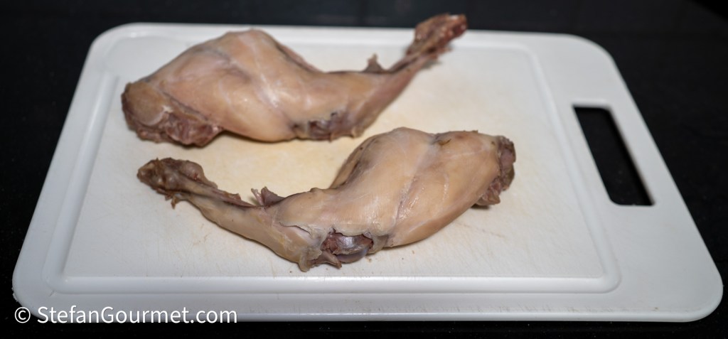 Two rabbit legs resting on a cutting board.
