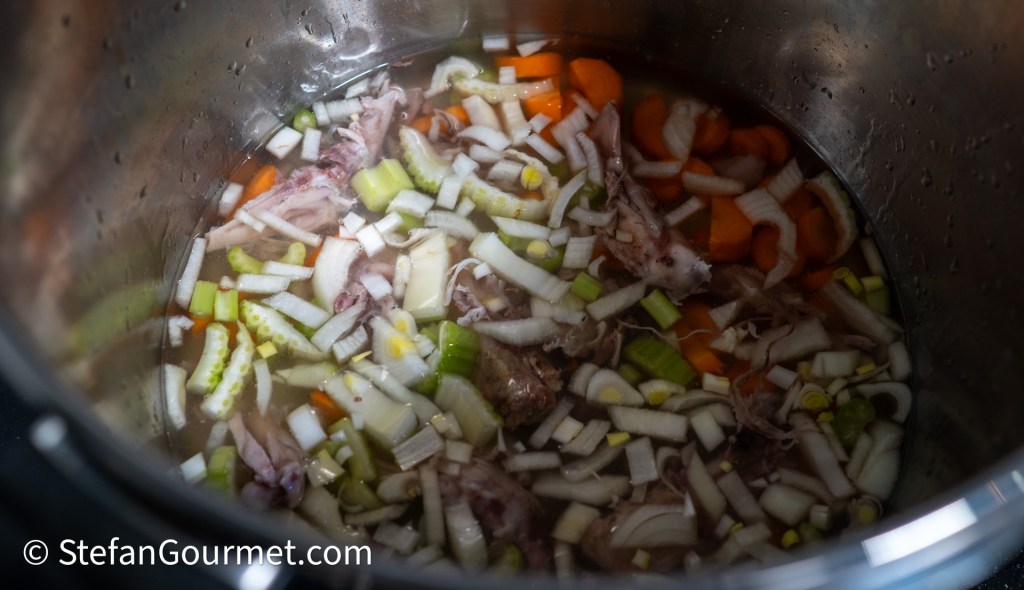 A pot filled with chopped vegetables such as carrots, celery, and onions, along with rabbit pieces, submerged in water for making stock.