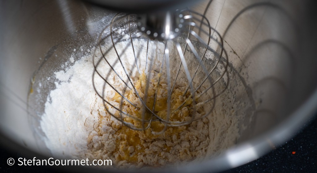Mixing ingredients for girini batter in a mixing bowl, featuring flour and eggs.