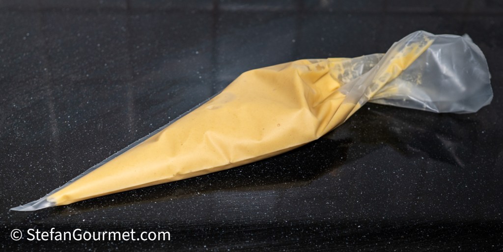 A piping bag filled with a yellow batter, resting on a black countertop.
