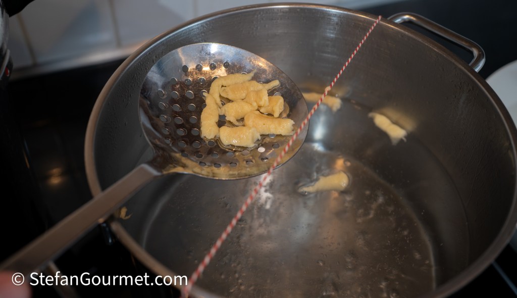 A slotted spoon lifting freshly cooked girini pasta from boiling water.