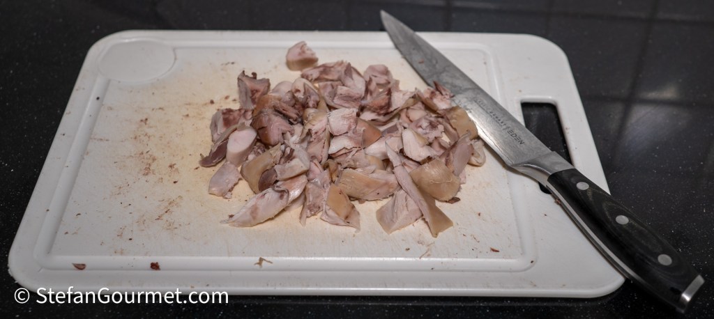 Chopped rabbit meat on a cutting board next to a knife.