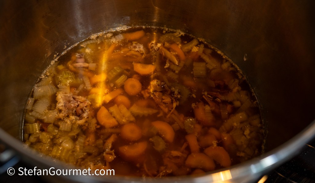 A pot filled with simmering rabbit stock made with carrot, celery, and herbs, showing a rich, amber liquid and chunks of vegetables.