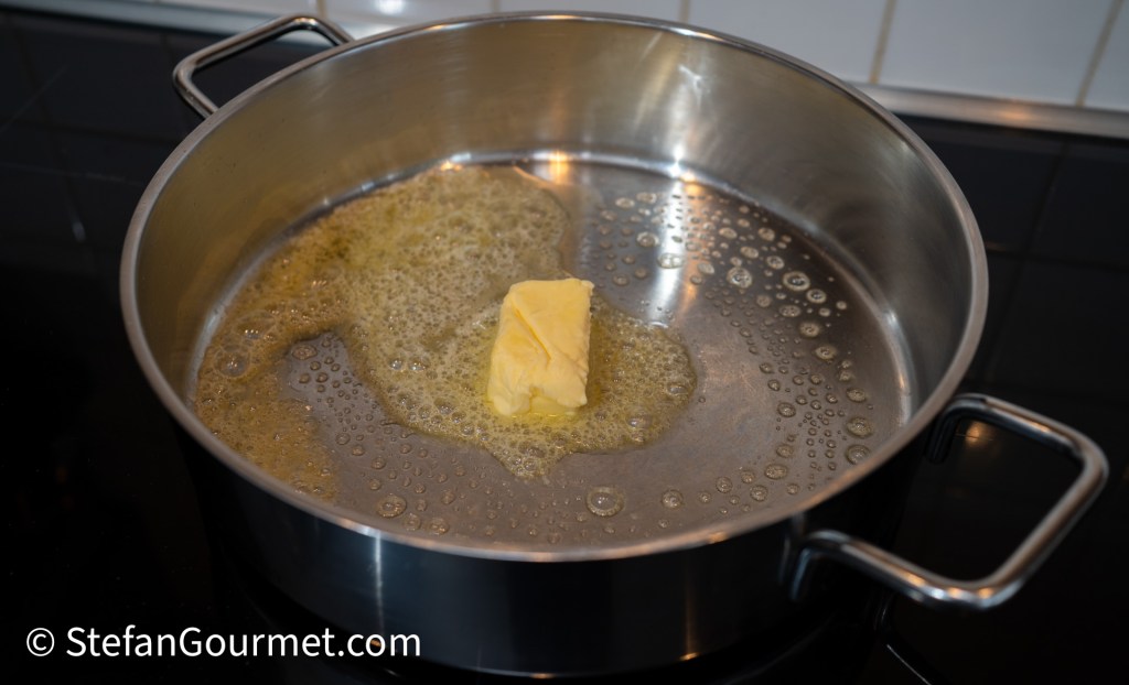 A silver pot with melted butter bubbling on a stovetop.