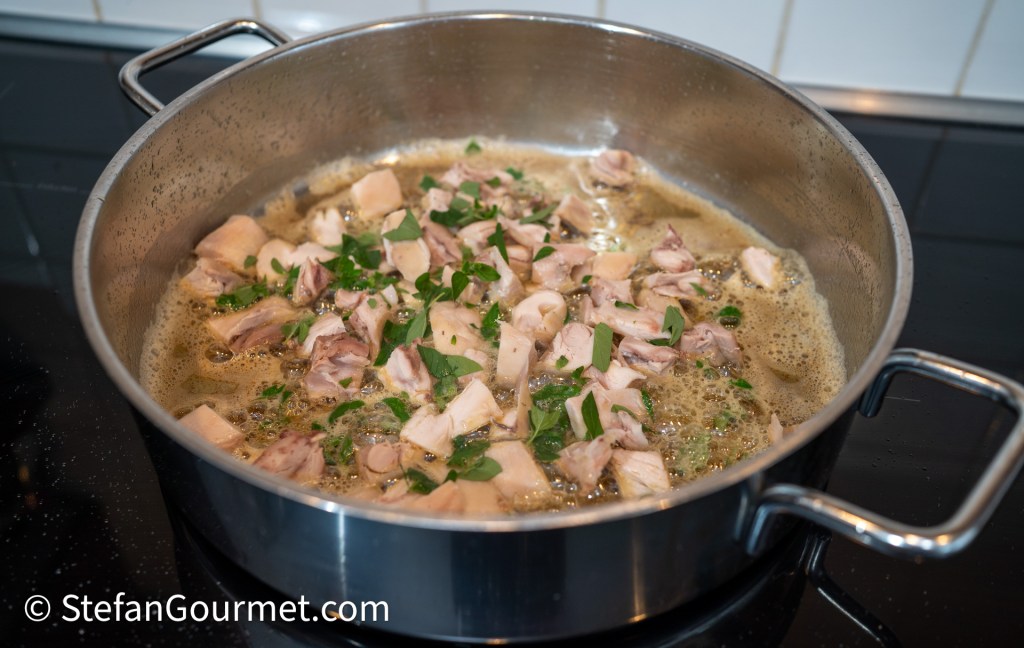 A pot with simmering chopped rabbit meat and herbs in a flavorful broth.