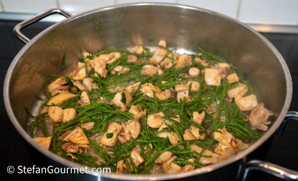 A pot filled with pieces of cooked rabbit meat and samphire, simmering together on the stove.