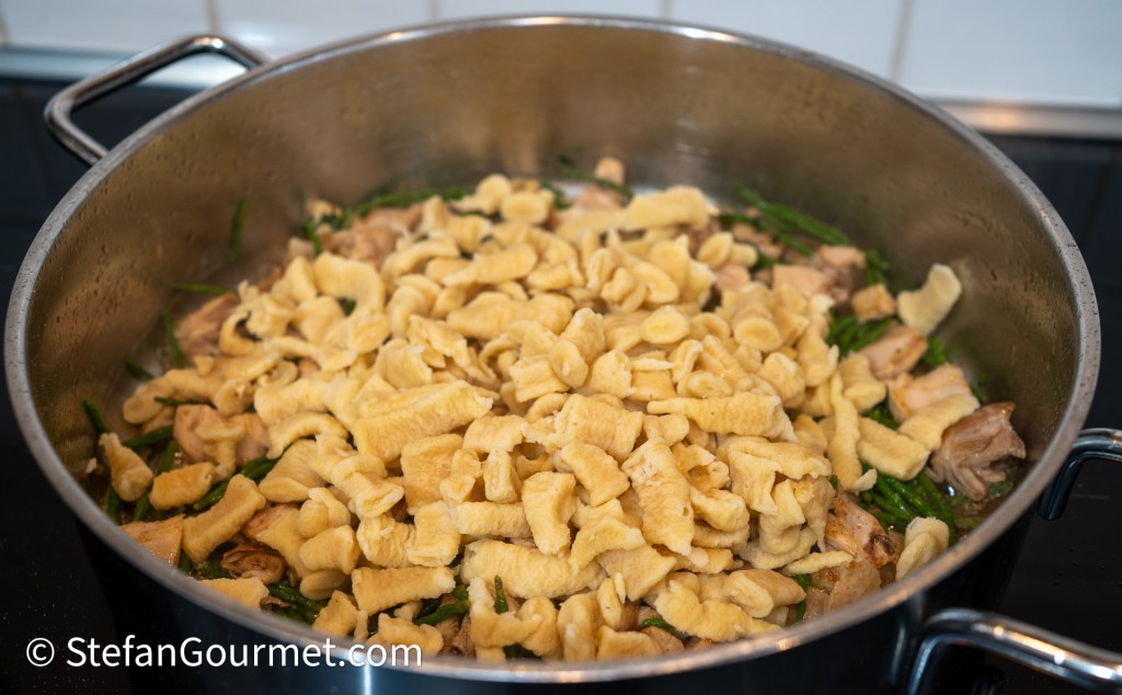A pot filled with freshly cooked girini pasta mixed with rabbit pieces and samphire greens.