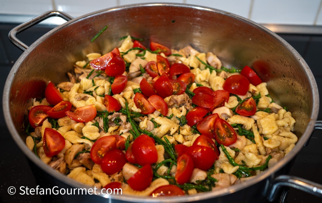 A pot filled with freshly prepared _girini_ pasta mixed with rabbit, cherry tomatoes, and wild greens, showcasing a colorful and hearty dish.