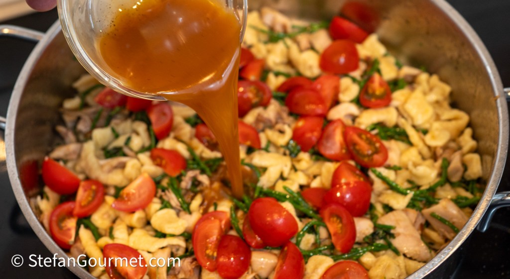 A pot of freshly cooked girini pasta mixed with rabbit meat, cherry tomatoes, and samphire, while a rich rabbit gravy is being poured on top.