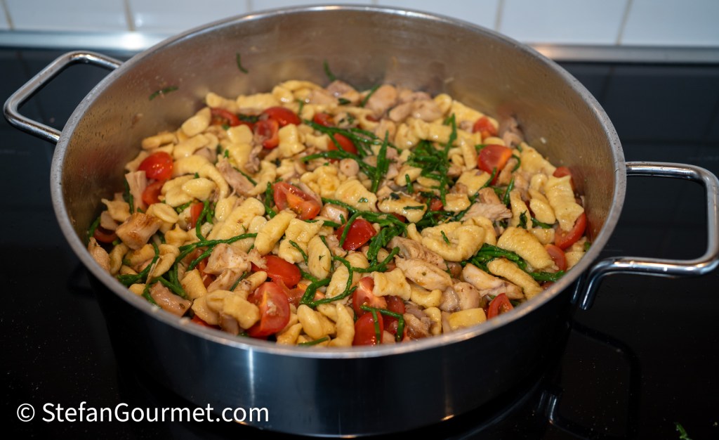 A pot filled with freshly cooked pasta mixed with rabbit, cherry tomatoes, and samphire, showcasing a colorful and rustic dish.