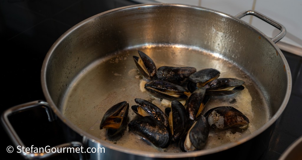 A pot with mussels cooking in a bit of liquid, showing some opened shells and steam rising.