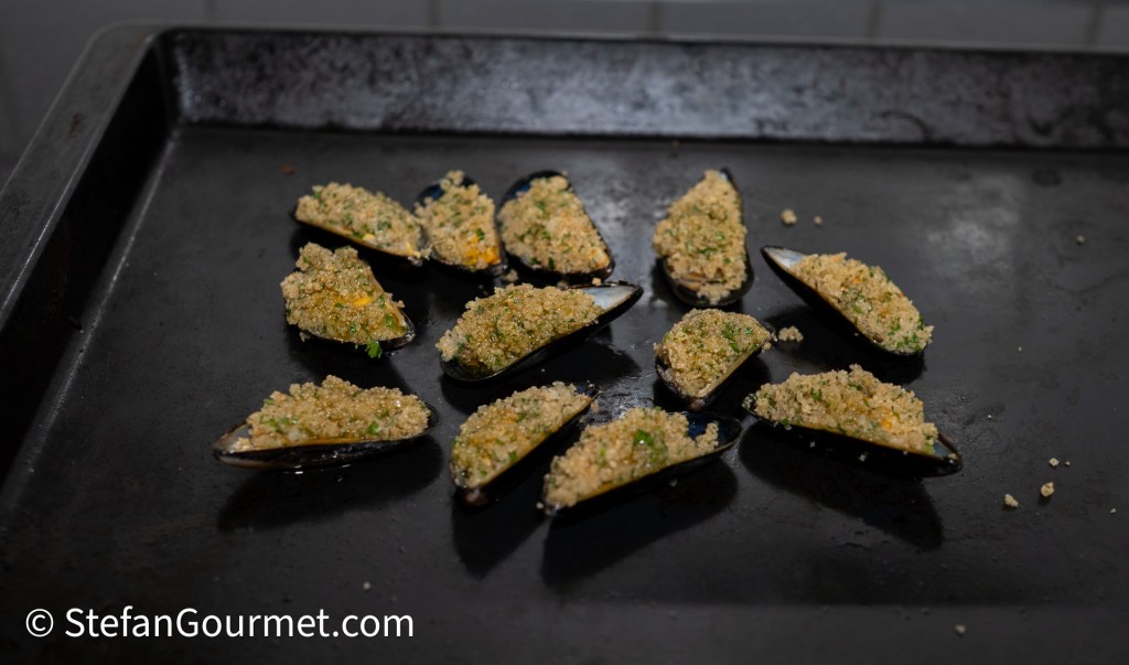 Baked mussels topped with breadcrumbs and herbs on a baking tray.