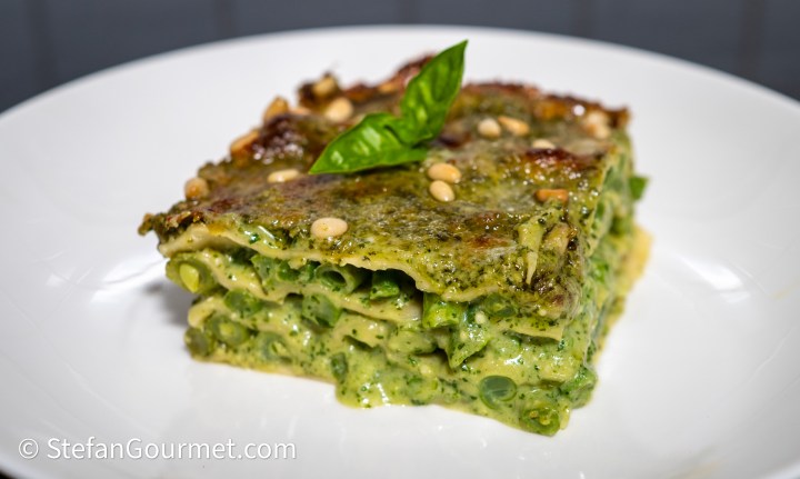A slice of lasagna alla genovese, layered with green beans and pesto, topped with pine nuts and a basil leaf.