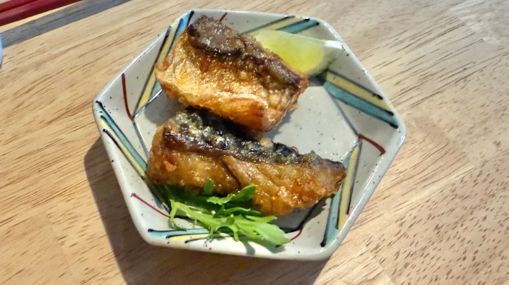 Two pieces of grilled mackerel served on a decorative plate with a slice of lime and some fresh greens.