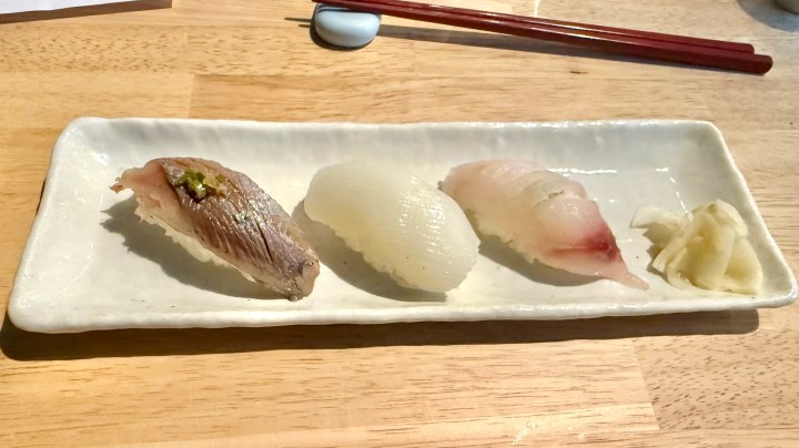 A plate of three pieces of sushi, featuring a variety of fish topped with wasabi, accompanied by pickled ginger.