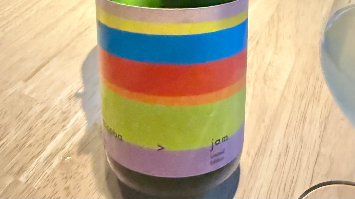 A bottle of sake labeled 'jam' with colorful horizontal stripes on a wooden table.