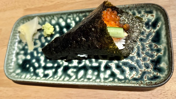 A temaki sushi cone with salmon roe, cucumber, and rice, served on a decorative blue plate alongside pickled ginger and wasabi.