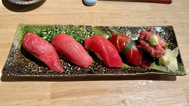 A plate of assorted nigiri sushi featuring five pieces of different types of tuna, including lean, medium-fatty, and fatty tuna, garnished with wasabi, pickled ginger, and served on a decorative green and black plate.