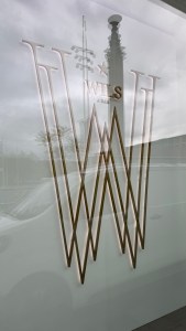 Exterior view of Wils restaurant featuring its logo on the window, with the reflection of the Olympic Stadium tower visible.