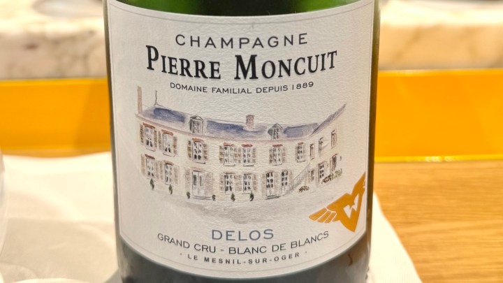 Close-up of a bottle of Champagne Pierre Moncuit from the Delos vineyard, featuring an illustrated label depicting the winery's picturesque exterior.
