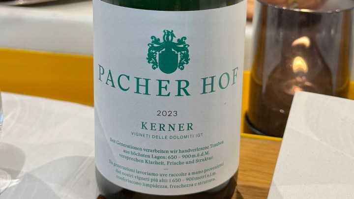 A close-up of a wine bottle labeled PACHER HOF KERNER 2023, placed on a restaurant table next to a candle.