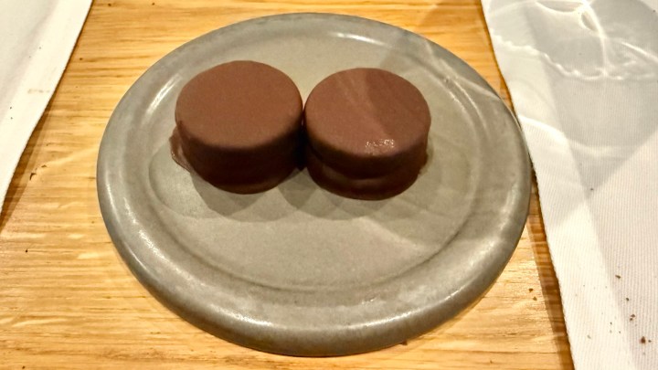 Two round chocolate desserts served on a gray plate, set on a wooden table.