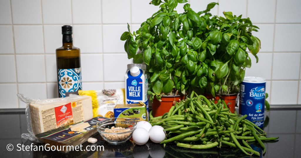 Ingredients for pesto alla genovese and lasagna, including fresh basil, green beans, eggs, cheese, olive oil, and milk on a kitchen counter.
