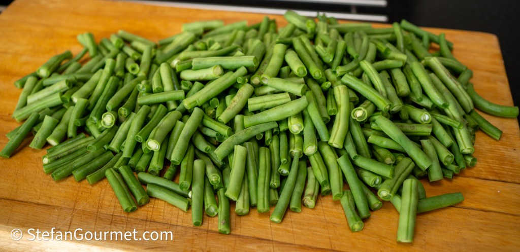 A large mound of trimmed green beans on a wooden cutting board.