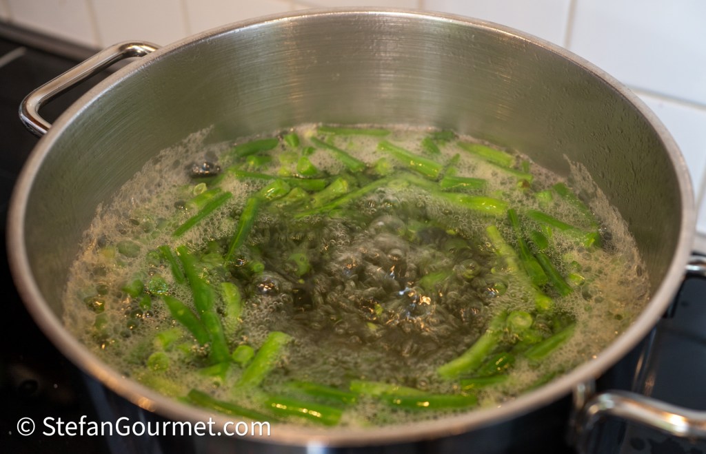 A pot of boiling water with chopped green beans cooking in it.