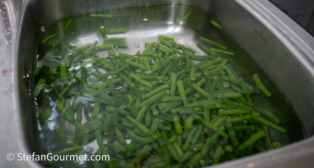 Fresh green beans soaking in water in a stainless steel sink.