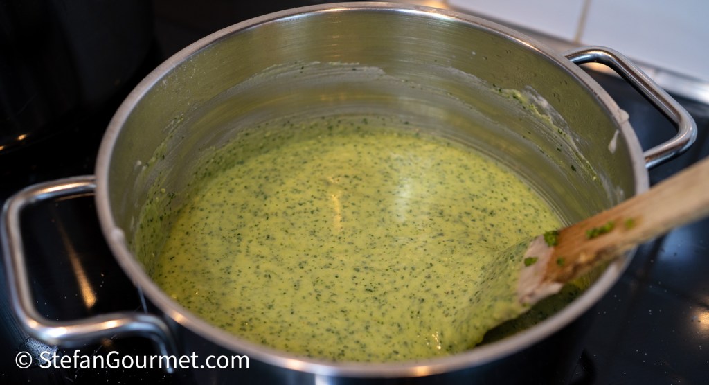 A pot filled with a green pesto sauce being stirred with a wooden spoon.