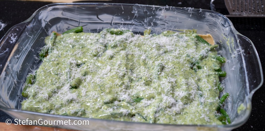 A glass baking dish filled with layers of green beans and pesto, topped with freshly grated cheese.