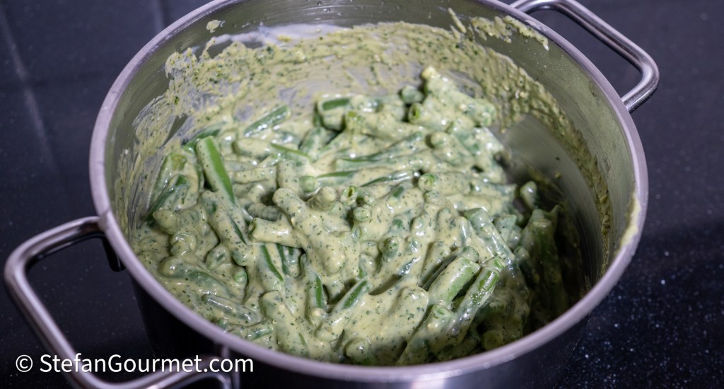 A pot filled with green beans mixed in a creamy pesto sauce.