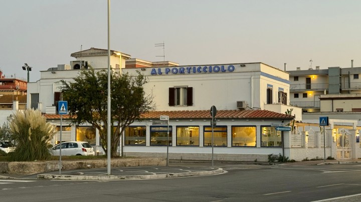 Exterior view of the restaurant 'Al Porticciolo' located in Fiumicino, Italy, showcasing its sign and surrounding area.