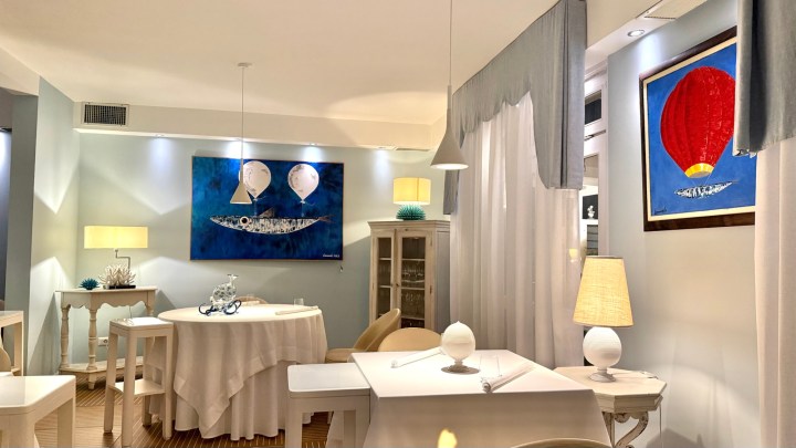 Interior of a seafood restaurant featuring white tables, a blue wall art piece with fish and balloons, and warm lighting.