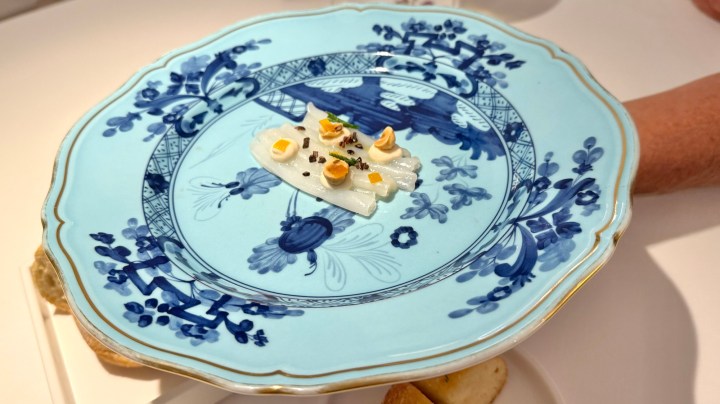 A beautifully presented dish on a blue and white porcelain plate, featuring a delicate seafood preparation with garnishes like yellow pieces and nuts.
