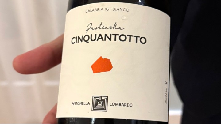 A close-up of a wine bottle labeled 'Particella Cinquantotto' by Antonella Lombardo, featuring a white background with an orange geometric design.
