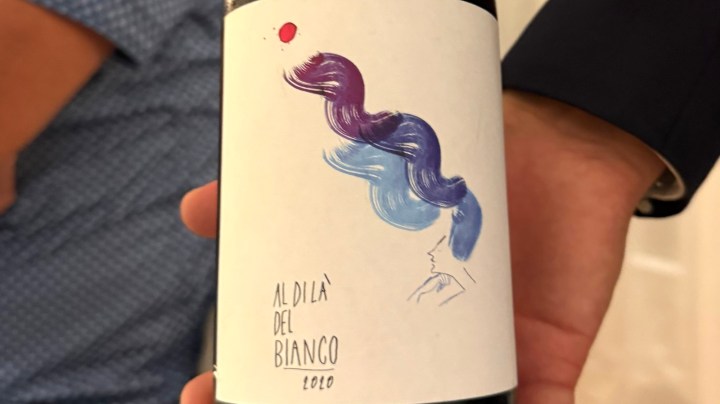 A close-up of a wine bottle featuring an artistic label with colorful hair-like designs and the text 'Al di là del Bianco 2020' beneath it.