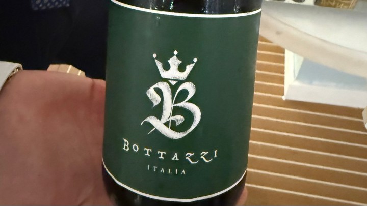 A hand holding a green wine bottle labeled 'Bottazzi' with a crown design and the word 'Italia' at the bottom.