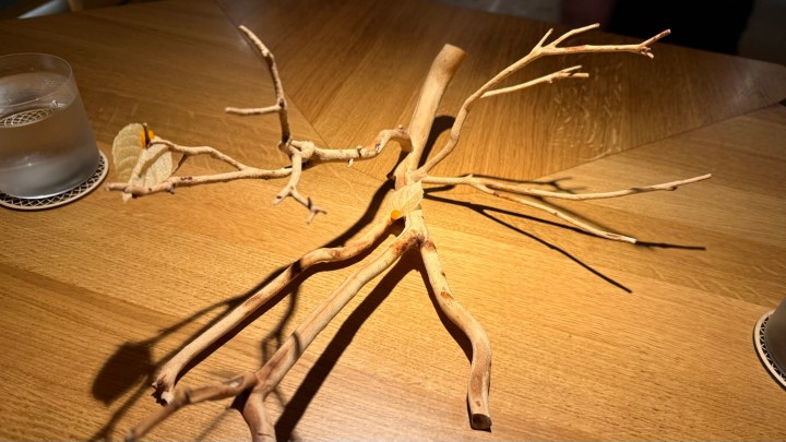 An artistic wooden branch sculpture placed on a dining table, surrounded by restaurant decor.