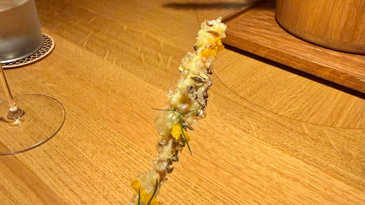 A creatively presented culinary dish on a wooden table, featuring delicate ingredients with vibrant garnishes, showcasing an artistic arrangement.