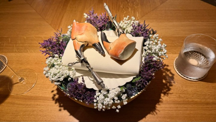 A decorative presentation of crab claws on a plate, surrounded by purple flowers and white baby's breath, with utensils placed elegantly on top.