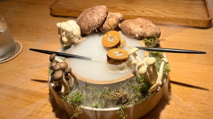 A beautifully presented dish featuring various mushrooms and a delicate dessert, presented with smoke and accompanied by chopsticks, on a wooden table.