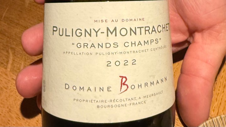 Close-up of a hand holding a bottle of 2022 Puligny-Montrachet 'Grands Champs' from Domaine Bohrmann.